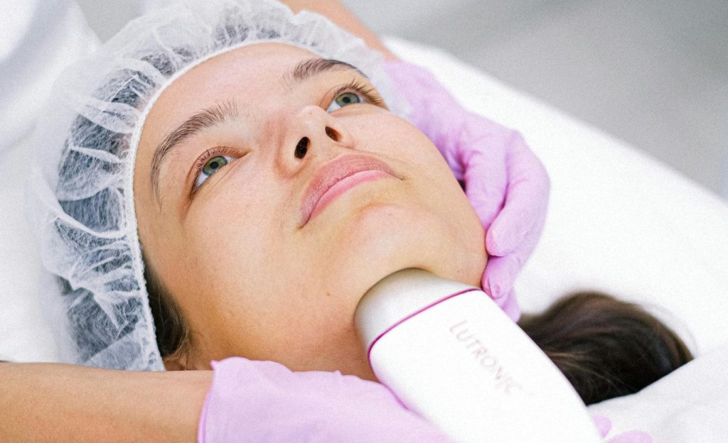 A cosmetologist performs a facial laser treatment on a young woman.